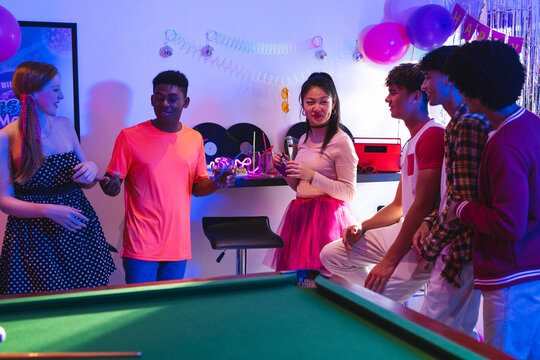 Teenagers enjoying lively party with drinks and laughter around pool table - Powered by Adobe