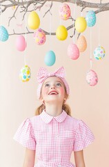 Delighted girl gazing at colorful easter eggs hanging from a tree branch against a pastel background, perfect for seasonal celebrations and joyful moments