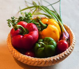 Colorful bell peppers, tomatoes, and herbs in a traditional woven basket.