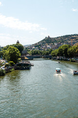 Serene river view with boats passing by in a vibrant city near the hillside during a sunny day
