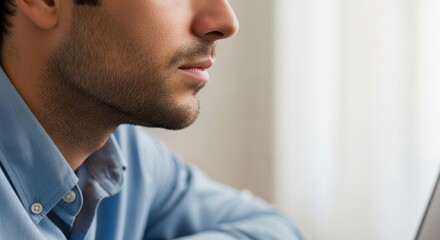 Fototapeta premium Profile of young caucasian male in blue shirt facing window light