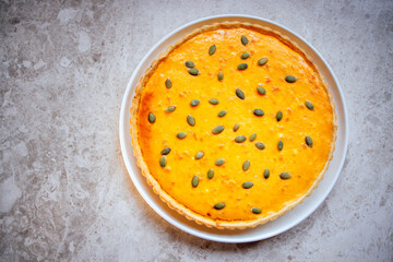 Delicious pumpkin pie topped with green pumpkin seeds, served on a white plate, showcasing a golden crust and smooth filling, perfect for autumn desserts and festive gatherings