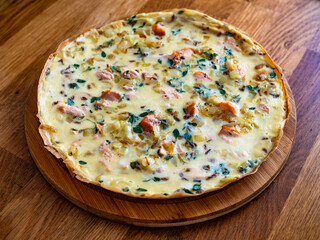 Frittata - scrambled eggs with roasted salmon bites, fried onion and fresh thyme on wooden table	