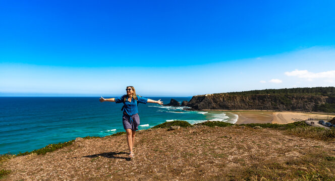 Beautiful mature woman tourist enjoying walk on cliff overlooking Odeceixe beach and ocean in summertime. Algarve Portugal. Front view