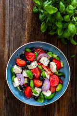 Greek style salad - tomatoes with feta cheese, basil leaves, red onion and black olives on wooden table	