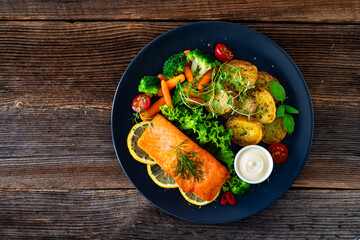 Fried salmon steak with boiled broccoli and mini carrots, fried potatoes and mayonnaise on wooden table	