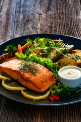 Fried salmon steak with boiled broccoli and mini carrots, fried potatoes and mayonnaise on wooden table	