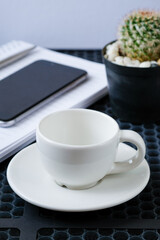 Empty coffee cup on desk with notebook smartphone and cactus for business planning