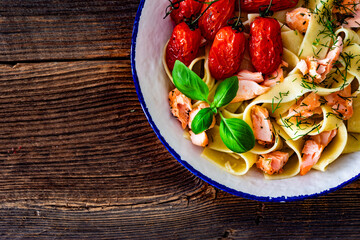Pasta with baked salmon, cherry tomatoes and dill on wooden table