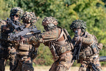 Fototapeta premium German Bundeswehr paratroopers in a NATO exercise assist an injured comrade, symbolizing teamwork, training, and military readiness.