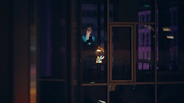 Night window businesswoman messaging smartphone in dim light. Late executive