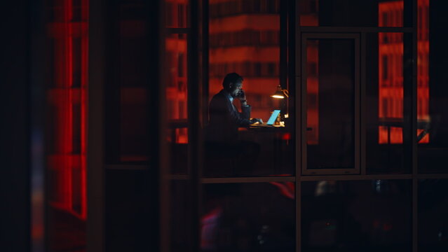 Night businessman silhouette window working alone at night talking smartphone