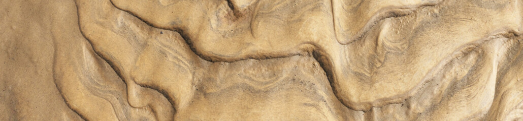 Close-up of natural sand ripple texture formed by wind and water. Abstract background with wavy layered patterns in warm beige and golden tones, ideal for use in design, texture, and creative backgrou
