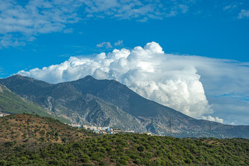 Mountain landscape in Morocco with lush green slopes, scattered villages, and dramatic white clouds...