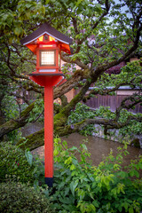 A traditional red japanese lantern on a post near a stream