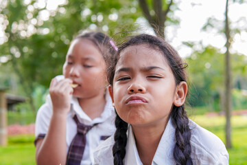 Elementary school girls in school uniform eating snacks and water. Her face looks happy and cheerful. They are sweating from playing and exercising. Concept of childhood fun, friendship, sharing.