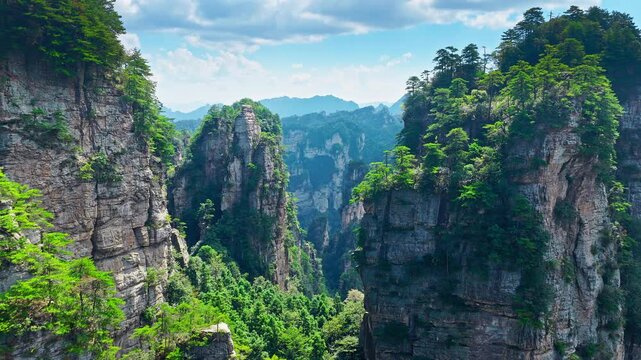 Aerial shot of stunning vertical karst mountain formations with green trees under a clear blue sky in Zhangjiajie National Forest Park, Hunan, China.