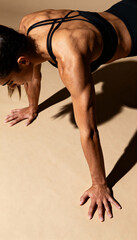 Naklejka premium female athlete model in sportswear holding a plank push-up position , toned muscles, studio backdrop