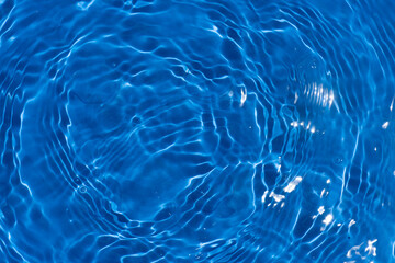 Blue water with ripples on the surface. Defocus blurred transparent blue colored clear calm water surface texture with splashes and bubbles. Water waves with shining pattern texture background.