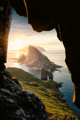 View out of a cave of Drangarnir, Tindholmur and Mykines during sunset. Stunning framed landscape shot.