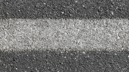 Fototapeta premium The asphalt surface shows a close-up of a lane marking with a distinct white stripe against a dark, gritty background. Daylight enhances the texture and contrast of the materials.