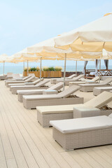 Sun beds loungers with umbrellas near swimming pool and beach at luxury resort. Sunny summer vacation.