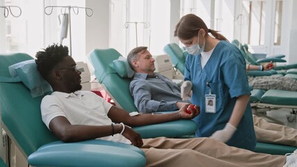 Young nurse in uniform attending to African American man donating blood in clean blood donation center