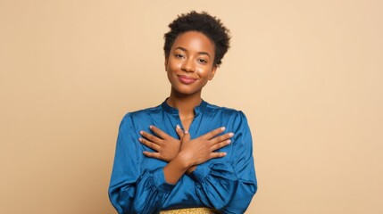 Obraz premium A young woman with a warm smile stands with her arms crossed in front of her chest, wearing a blue blouse. Her natural hair complements her confident demeanor, set against a soft beige backdrop.