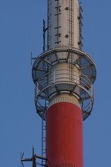 A vertical, low-angle shot of a tall red and white communication tower, with its various antennas and platforms visible against a clear blue sky.