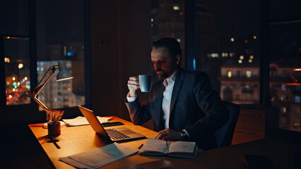 Overworked businessman enjoying cappuccino cup late evening workplace closeup