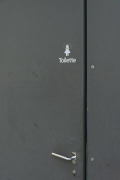 A minimalist female restroom sign, with a silhouette and the German word "Toilette" in white against a dark background, ideal for themes of travel, public spaces, and wayfinding.