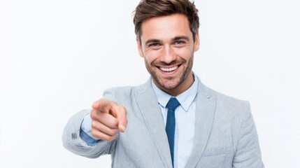 Naklejka premium A man dressed in a light gray suit with a blue tie smiles broadly while pointing directly at the viewer, suggesting an approachable and engaging demeanor.