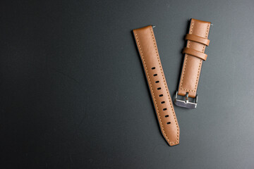 A brown leather watch strap on a black background, top view