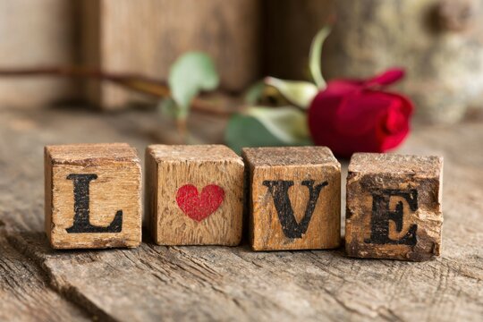 Wood blocks spell LOVE with a heart A red rose rests behind them on a rustic wooden surface