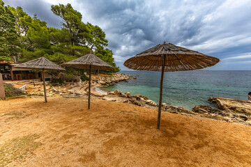 Tara Beach on the island of Rab, Straw sun umbrellas on the shore of the Adriatic Sea,