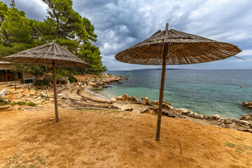 Tara Beach on the island of Rab, Straw sun umbrellas on the shore of the Adriatic Sea,