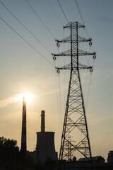 High voltage power lines and industrial plant with chimneys at sunset, symbolizing importance of reliable electricity infrastructure, energy distribution, technology, and sustainable urban development © Volha