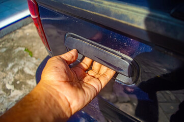 Hand reaching to open tailgate handle on dusty truck highlighting rugged use, outdoor wear, and practical interaction with vehicle surface in urban or work setting.