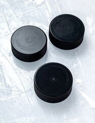 Three black hockey pucks on ice (1)