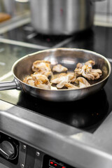 Oyster mushrooms sautéing in a stainless steel frying pan on a modern electric stovetop in a professional kitchen setting. Cooking process, food preparation, culinary concept.
