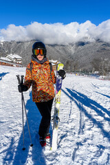 A female skier with skis in front of snow-covered mountains, ready to descend.