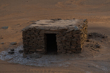Small stone hut in Morocco Sahara desert built from stacked rocks standing alone on sandy ground...