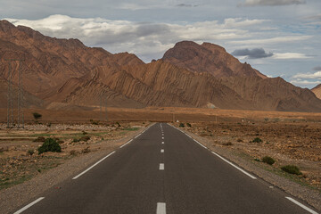Atlas Mountains Morocco desert road winding through rocky hills with dry landscape and blue sky above
