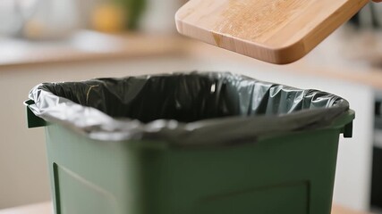 Vegetable scraps being discarded into a green trash bin in a kitchen setting.