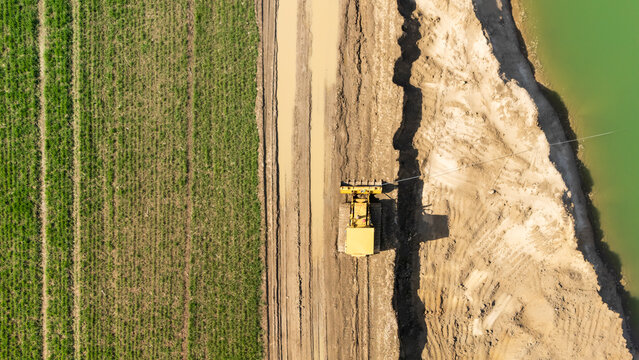 Aerial view of a yellow bulldozer working in a field separating cultivated land from a water body. Soil preparation and land use in agriculture and construction.