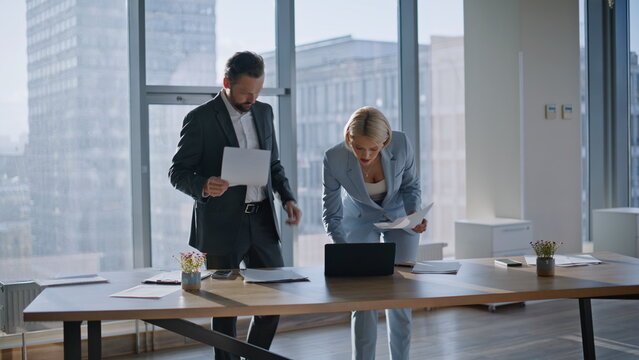 Smiling coworkers discussing papers in cityscape office. Brokers checking report