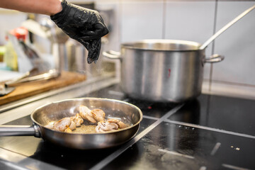 Chef seasoning sliced mushrooms in a hot frying pan on electric stove. Steam rises as cooking progresses in a professional kitchen with stainless steel cookware