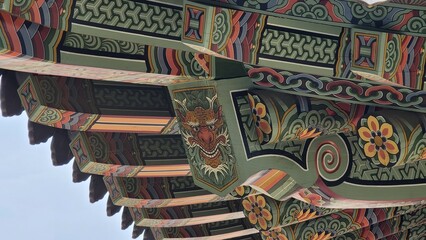 Obraz premium Traditional Korean temple architecture with vibrant dancheong patterns on eaves and roofs, showcasing colorful wooden details against blue sky and nature.