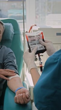 Vertical shot of over the shoulder shot of unrecognizable nurse in gloves checking quality of blood bag after donation in clinic