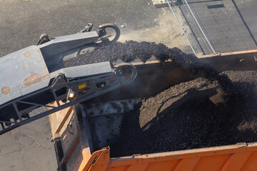 An overhead shot of an orange dump truck receiving asphalt from a conveyor on a road. This image is...